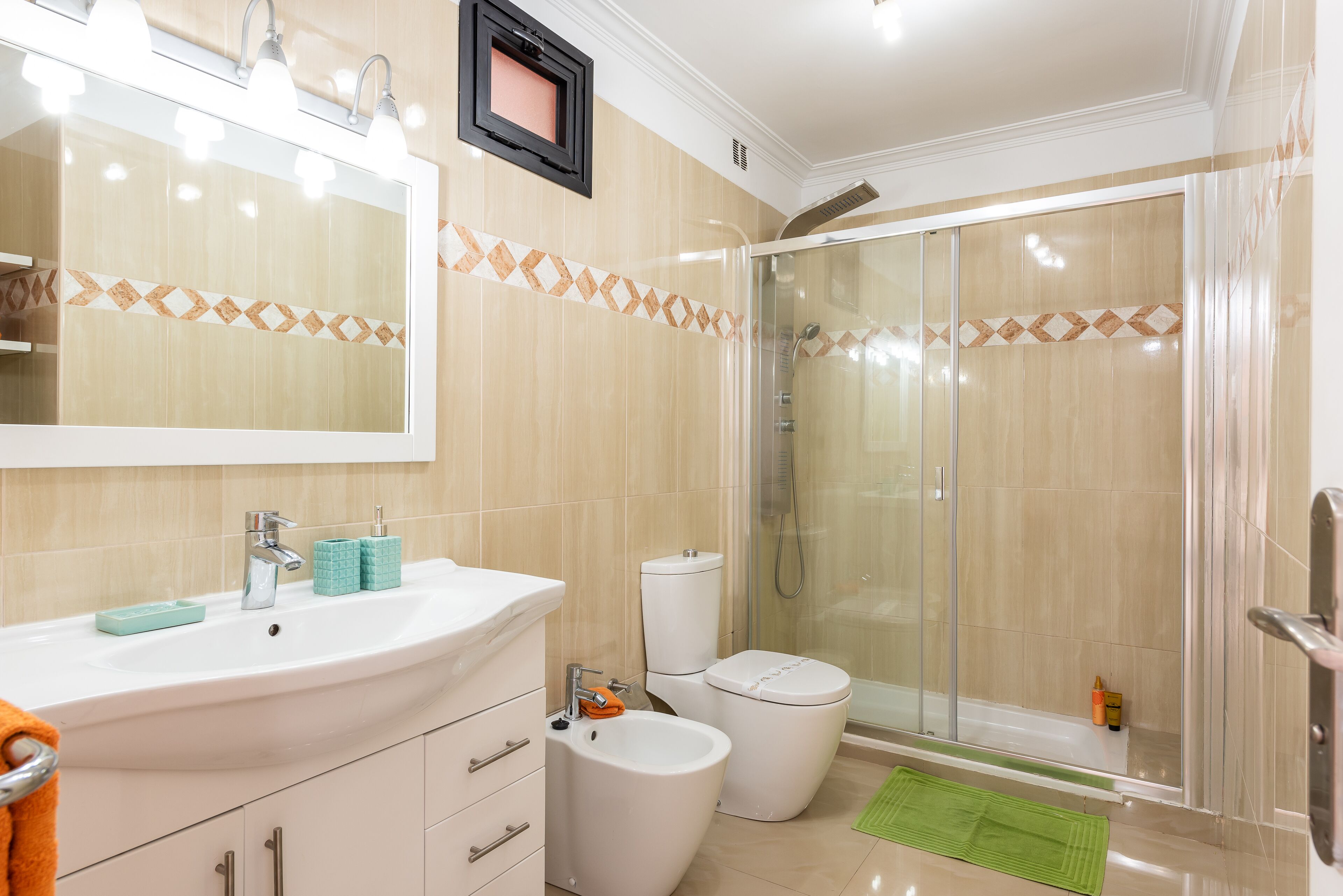 A modern bathroom with a large mirror, a sink, a bidet, a toilet, and a glass-enclosed shower.