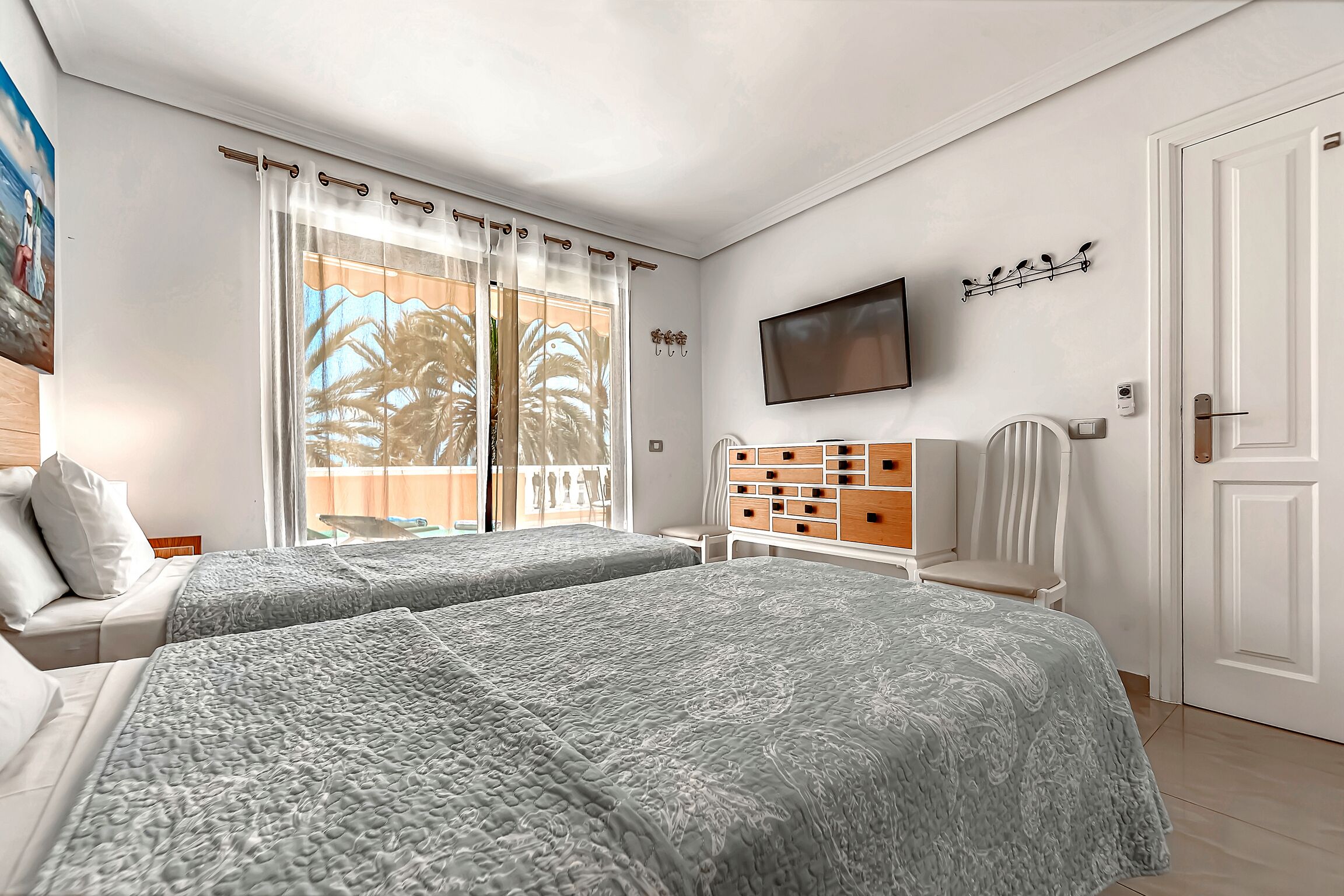 Habitación de hotel con dos camas, televisión, una silla, un mueble bajo para televisión con cajones y una puerta.