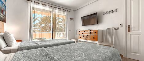 Habitación de hotel con dos camas, televisión, una silla, un mueble bajo para televisión con cajones y una puerta.