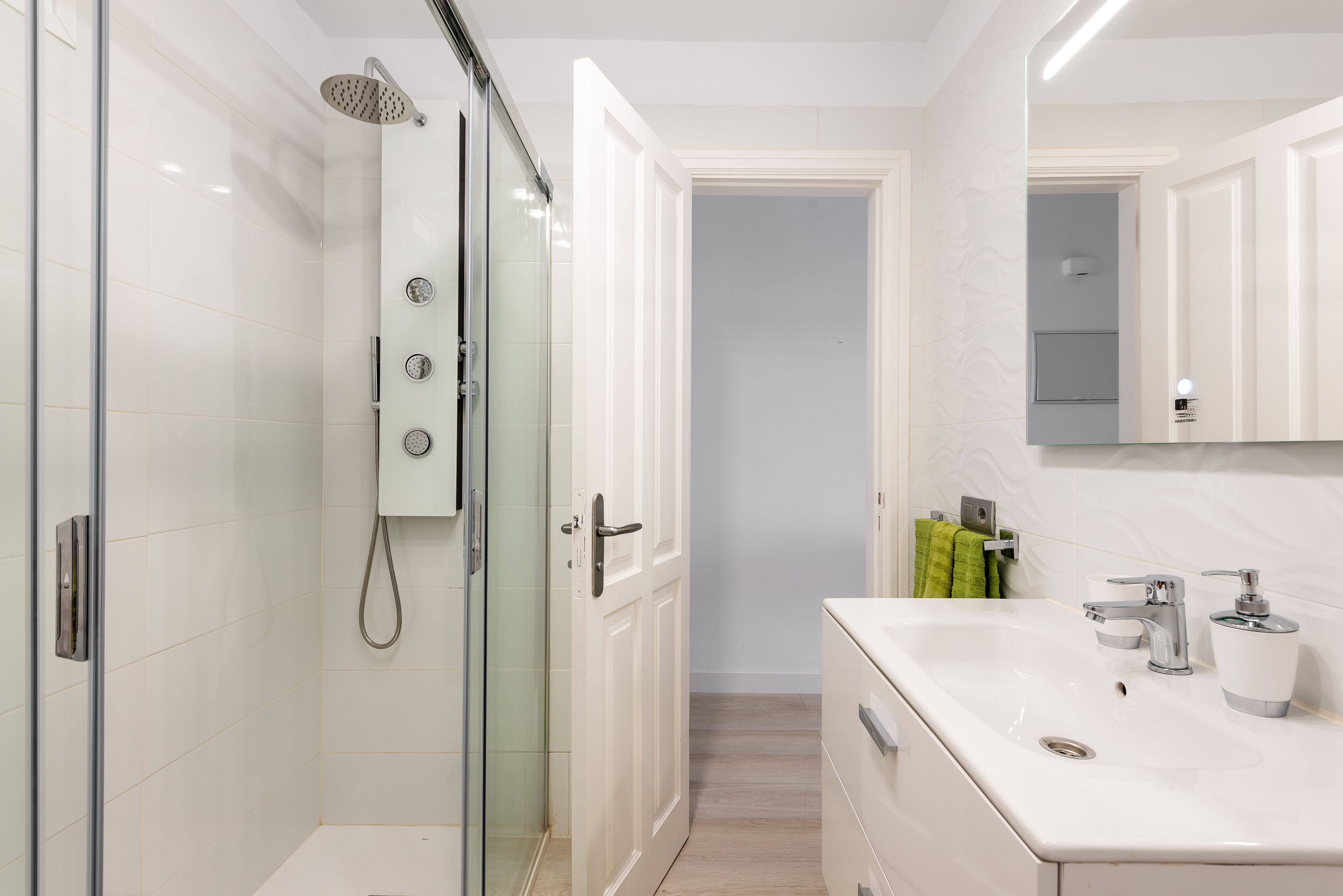 A modern bathroom with a glass-enclosed shower, a white sink with a mirror, and a door leading to another room.