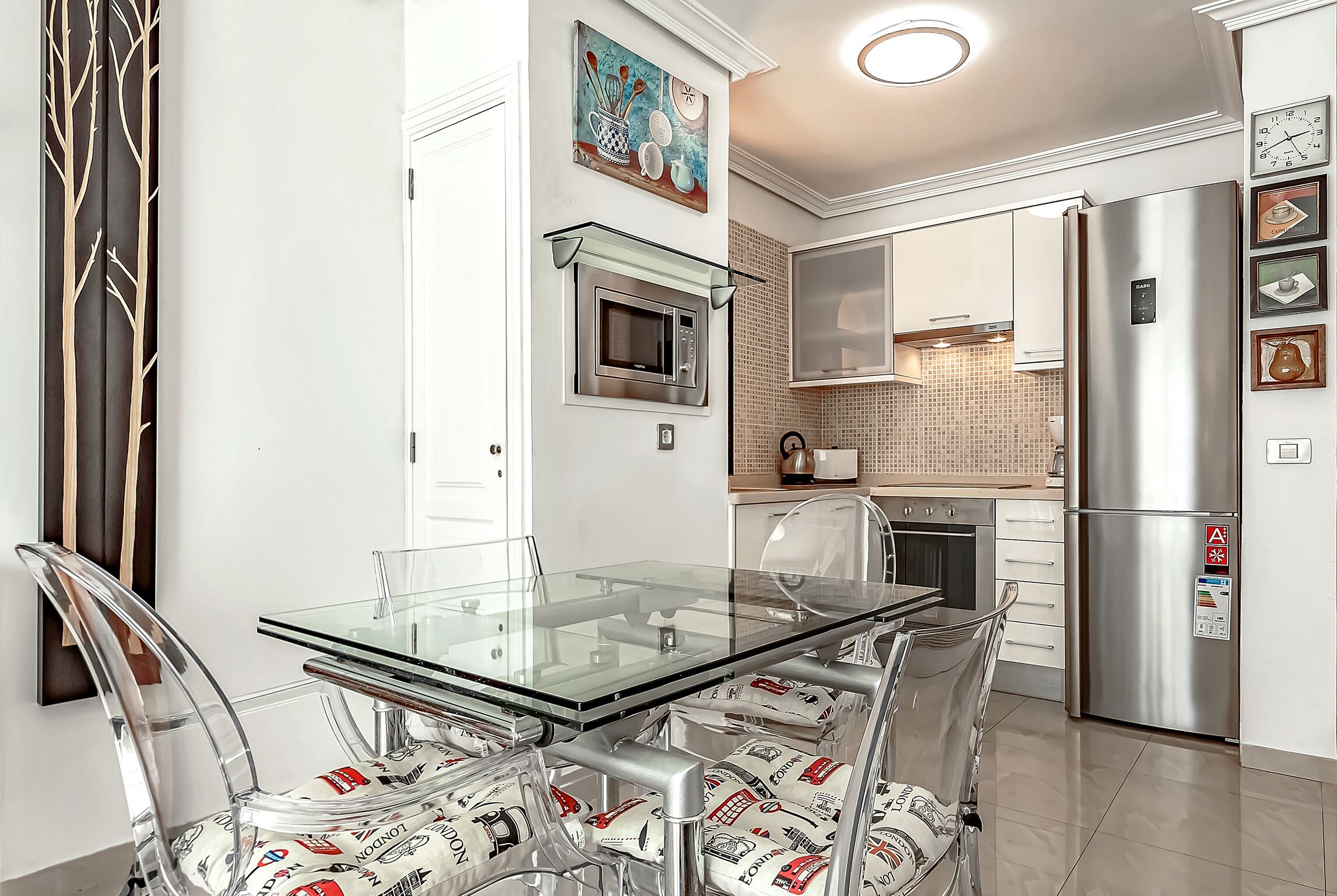 Una cocina moderna con una mesa de comedor de vidrio, electrodomésticos de acero inoxidable y sillas traslúcidas con cojines estampados.