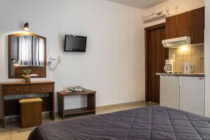 A bedroom with a bed, a desk, a television, and a kitchenette. - Golden Sun Kokkari (Samos)