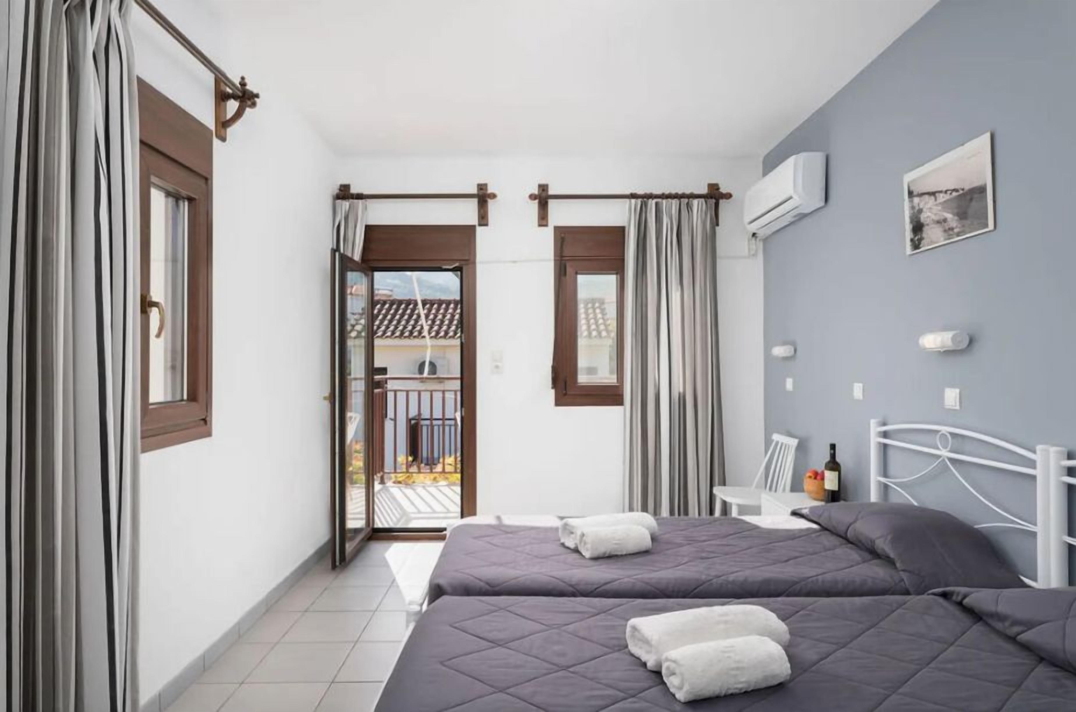 A bedroom with two beds, a balcony, and a view of the outside.
