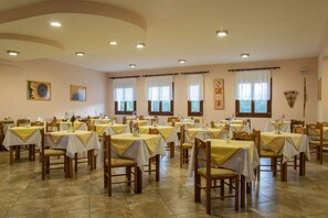 A dining area with multiple tables, chairs, and ceiling lights. - Golden Sun Kokkari (Samos)