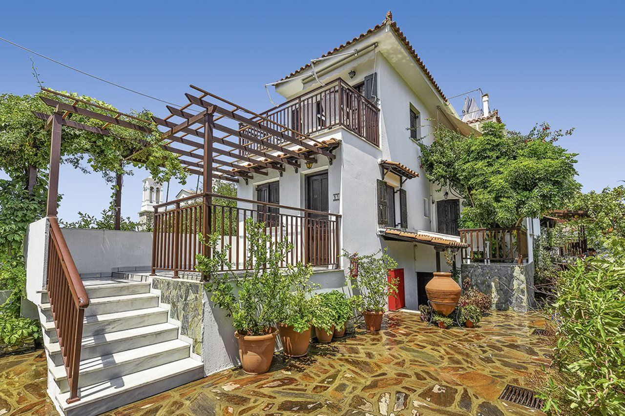 A two-story house with a stone-paved courtyard, a wooden pergola, and a staircase leading to the entrance.