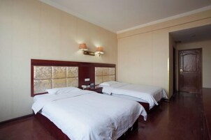 Una habitación de hotel con dos camas individuales, un cabecero de madera, una mesita de noche y una lámpara fijada a la pared.