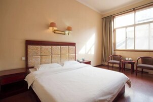Habitación de hotel con una cama grande, dos mesitas de noche, una ventana con cortinas y dos sillones.