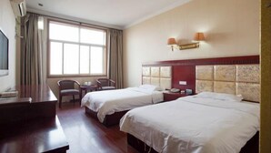 Een hotelkamer met twee enkele bedden, een bureau, een stoel, een kleine tafel en een groot raam met gordijnen.