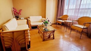 Ein Zimmer mit einer Couch, Sesseln, einem Couchtisch und einem Fenster mit Vorhängen.