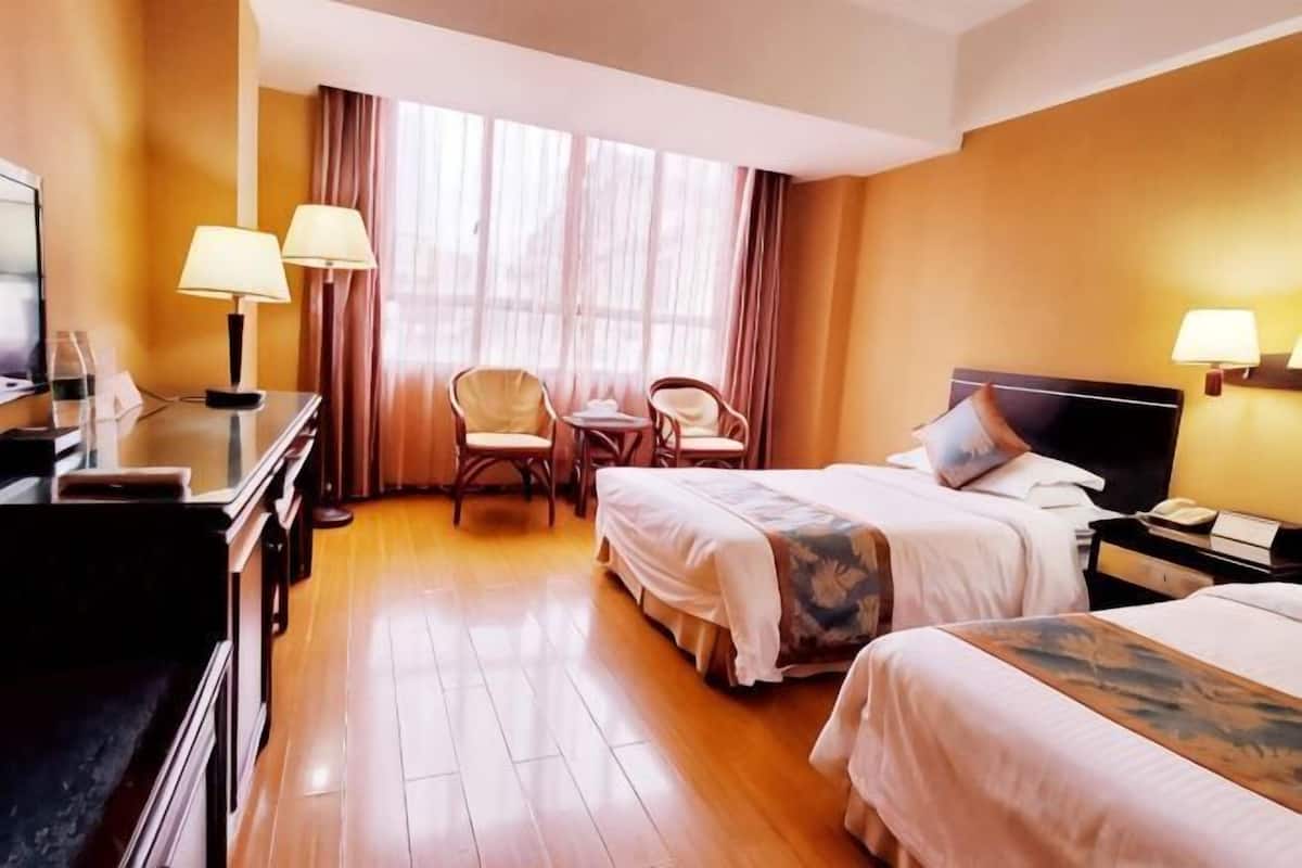 A hotel room with two beds, a desk, a chair, and a TV.