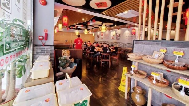 Ein Restaurantinneres mit Holzboden, hängenden Laternen und Bambusdekoration. Tische sind mit Essenden gedeckt.