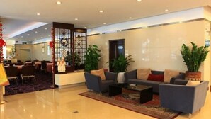 Eine Hotelhalle mit einer Rezeption, einer Sitzecke mit Sofas, Topfpflanzen und einem dekorativen Raumteiler.