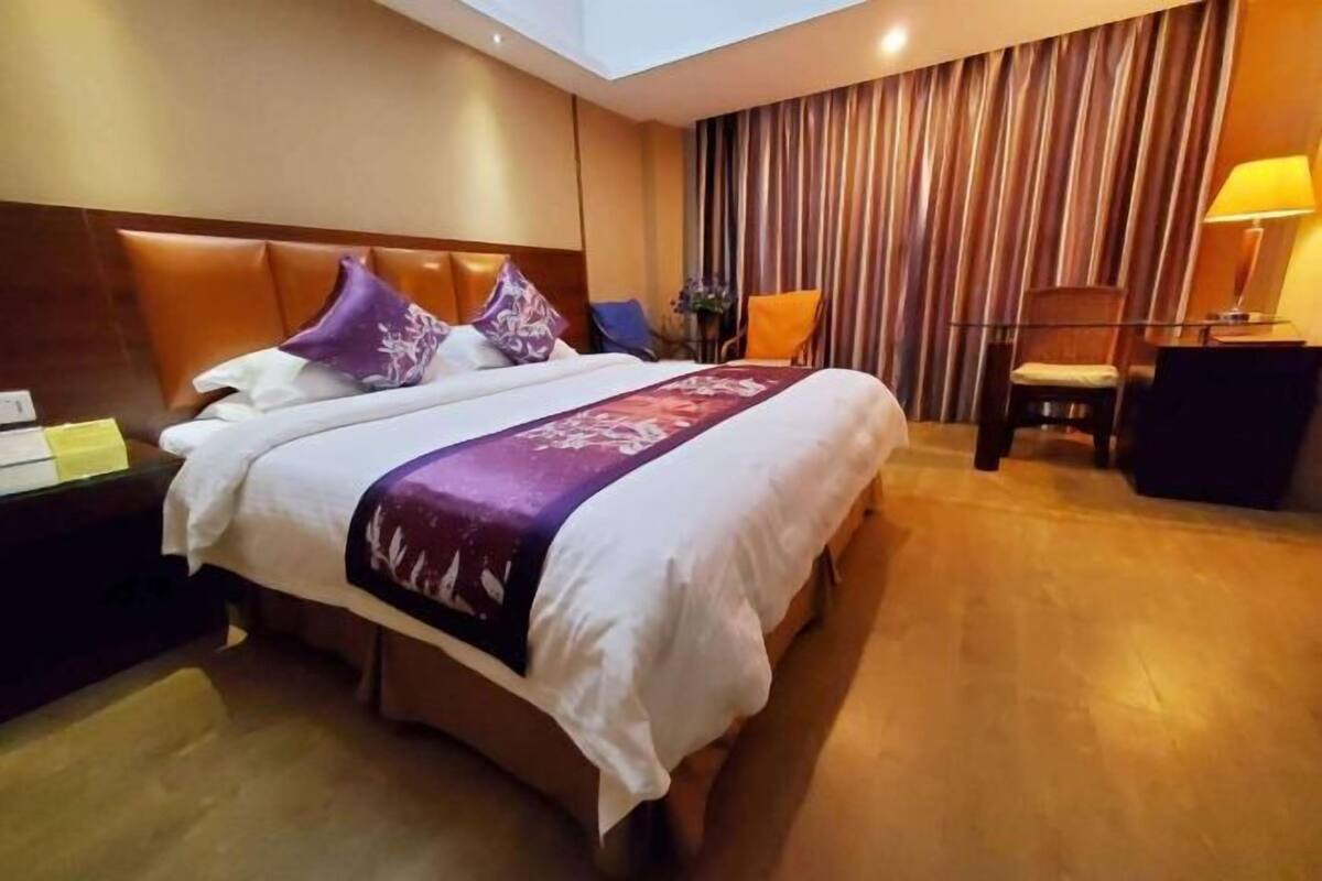 A hotel room with a large bed, a nightstand, a chair, a lamp, and a curtain.