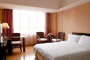 A hotel room with a bed, a desk with a lamp, two chairs, and a small table with a vase. - Hedong Hotel (Shenzhen)