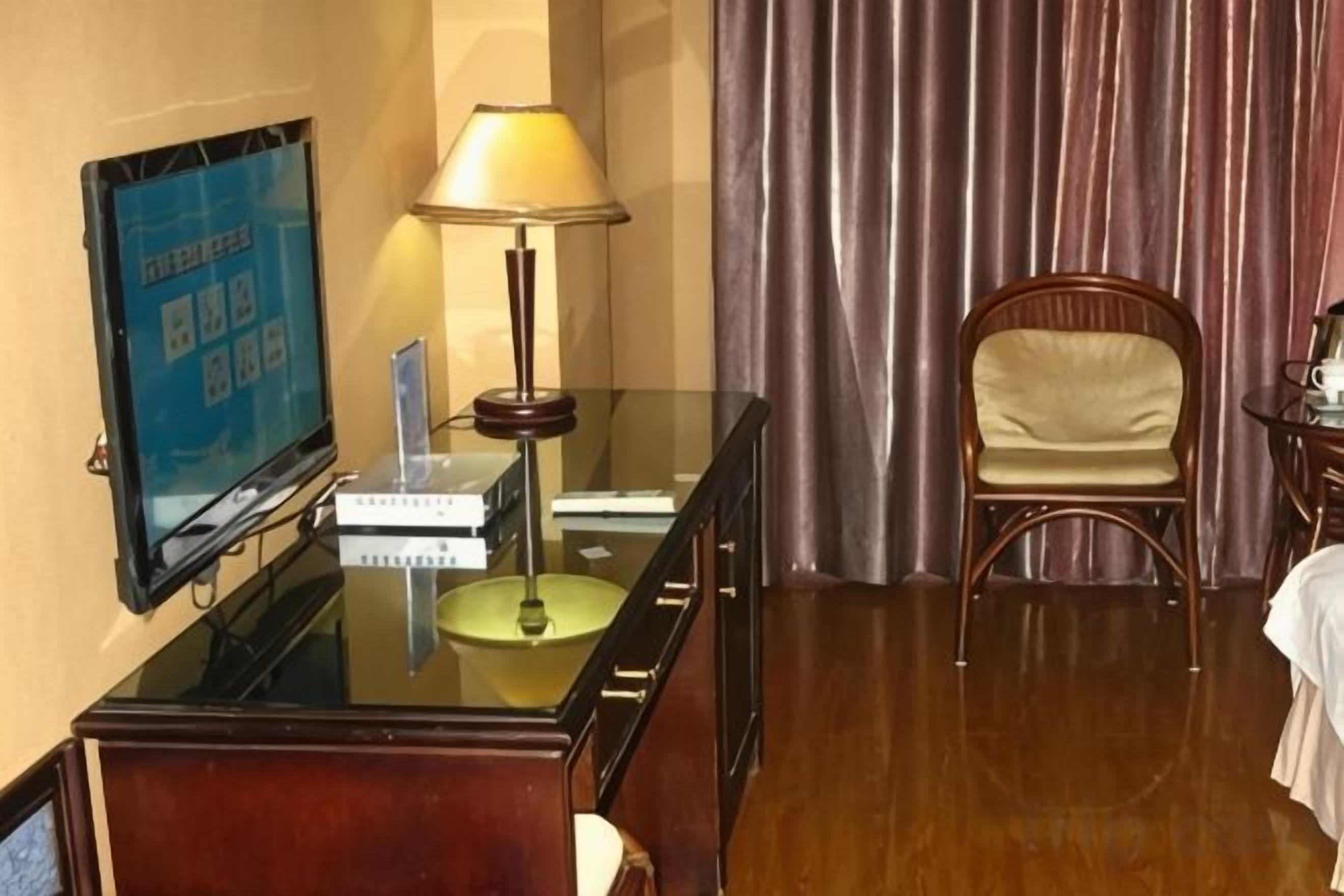 Una habitación de hotel con escritorio, televisor, lámpara, silla y cortina.