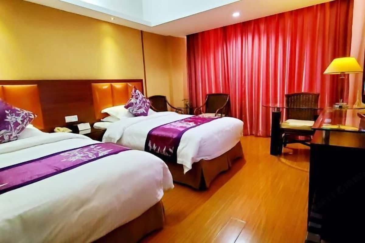 A hotel room with two beds, a desk, chairs, and a red curtain.