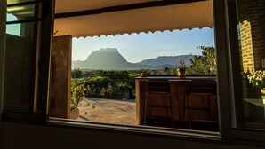 A view from a window with a metal chair and a table, overlooking a garden with potted plants and a mountain in the distance. - Phu Vara (Chiang Dao)