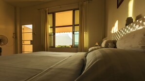 A bedroom with a large bed, a window with curtains, and a fan on the left. - Phu Vara (Chiang Dao)