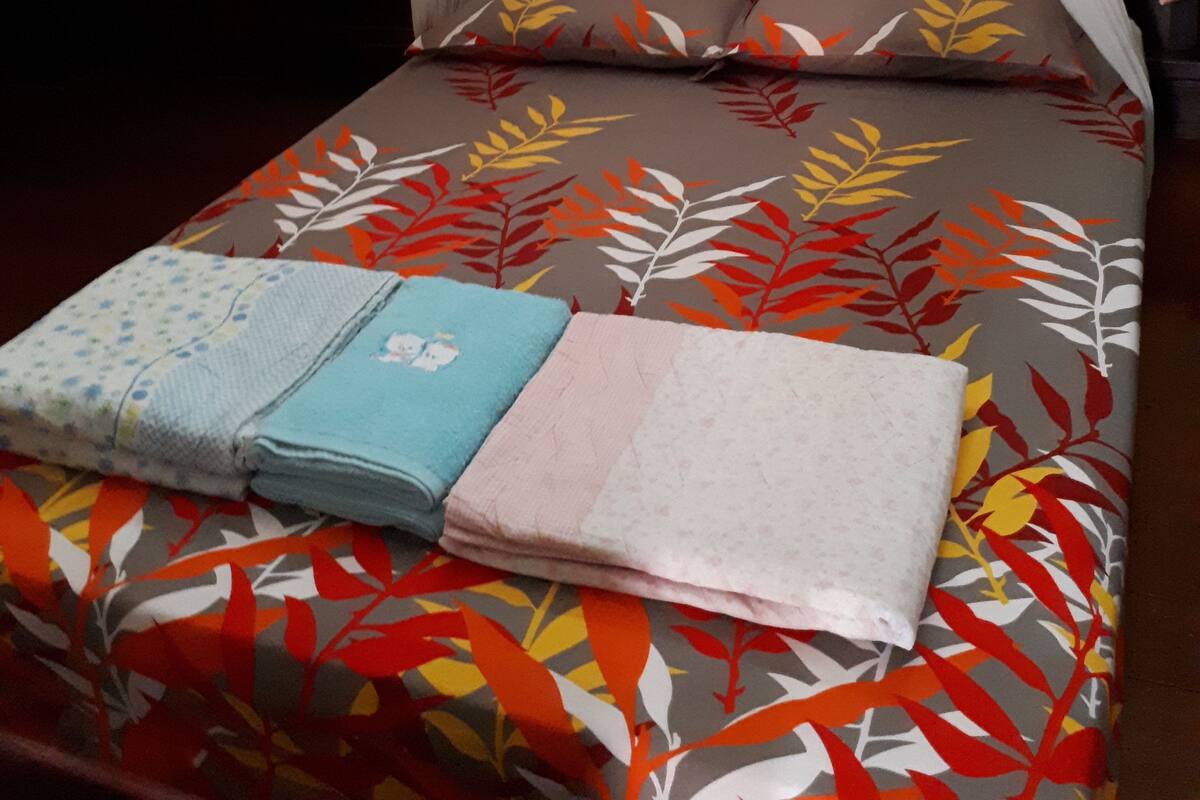 A bed with a canopy, pillows with leaf patterns, and folded towels.