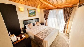 A bedroom with a wooden ceiling, a bed with a headboard, a nightstand, a lamp, and a painting on the wall.