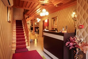 Zona de recepción de un hotel con una escalera de madera, un mostrador de recepción y un cartel indicador.