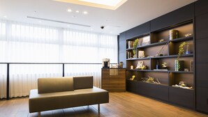 A modern living room with a sofa, wooden flooring, a large window with sheer curtains, and a built-in shelving unit with decorative items.