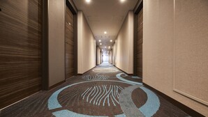 A hotel corridor with a patterned carpet, wooden doors, and recessed lighting.