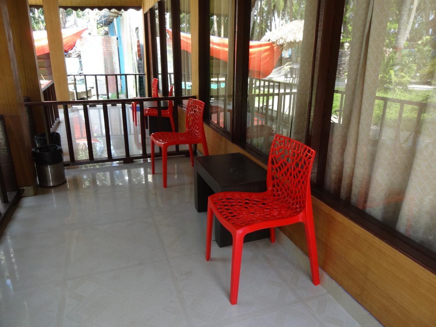 A balcony with red chairs and a table, large windows, and a view of the outside.