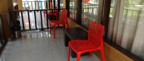 A balcony with red chairs and a table, large windows, and a view of the outside.