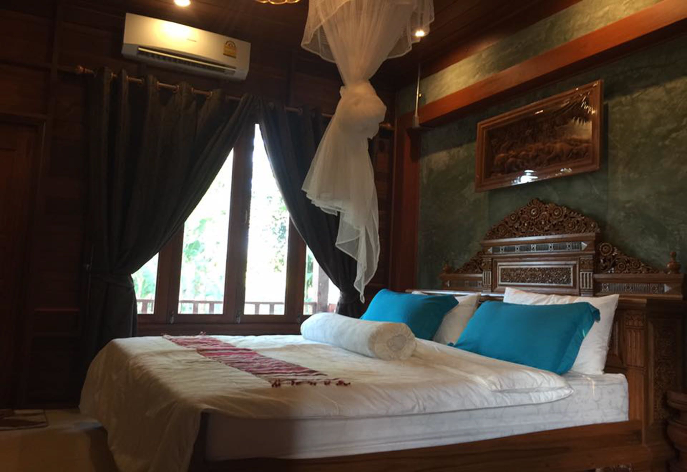 A bedroom with a bed, curtains, an air conditioning unit, a wooden headboard, and a wall-mounted picture.