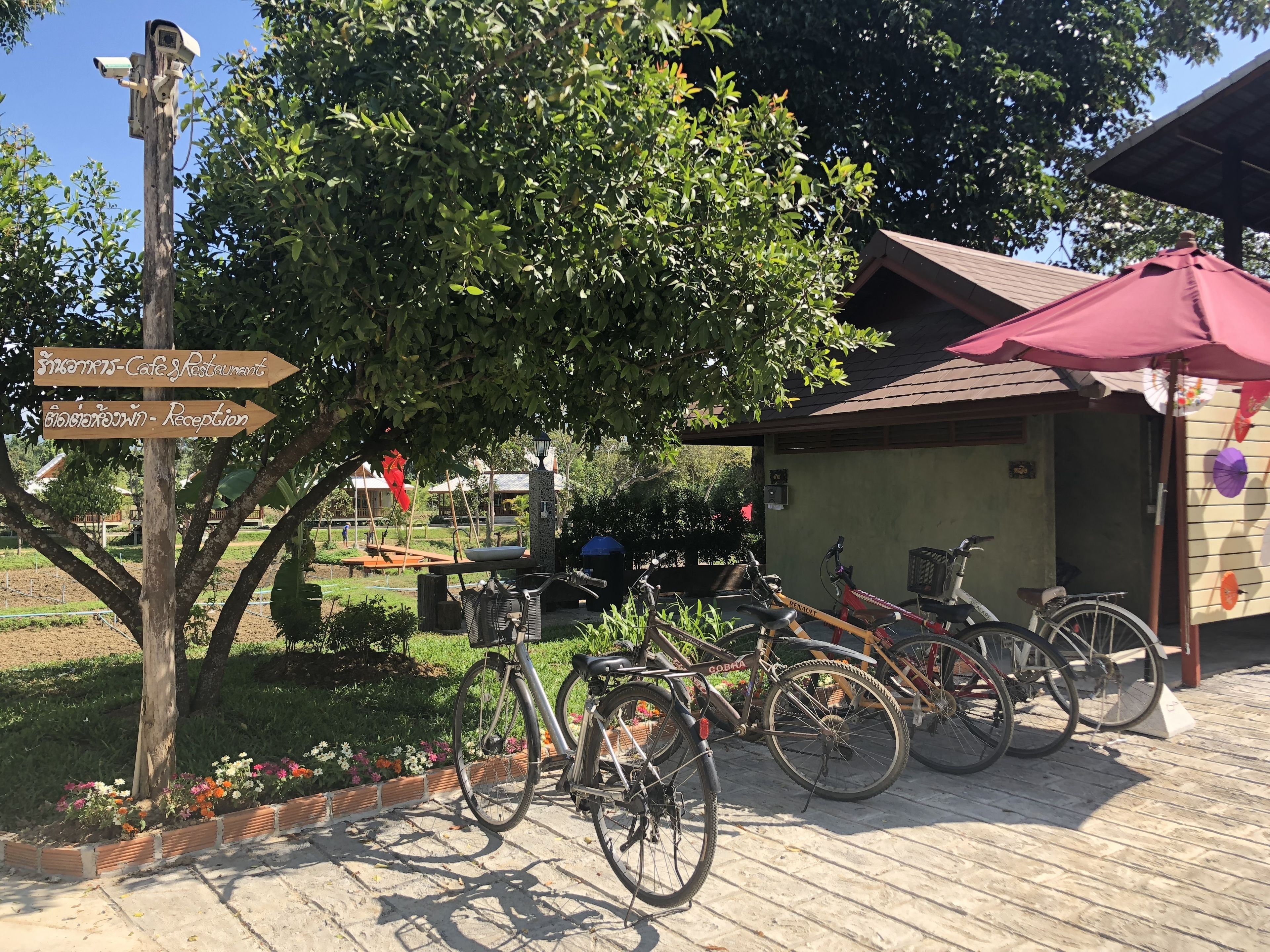 Zona de recepción con un letrero de madera, bicicletas y un edificio con una sombrilla roja.