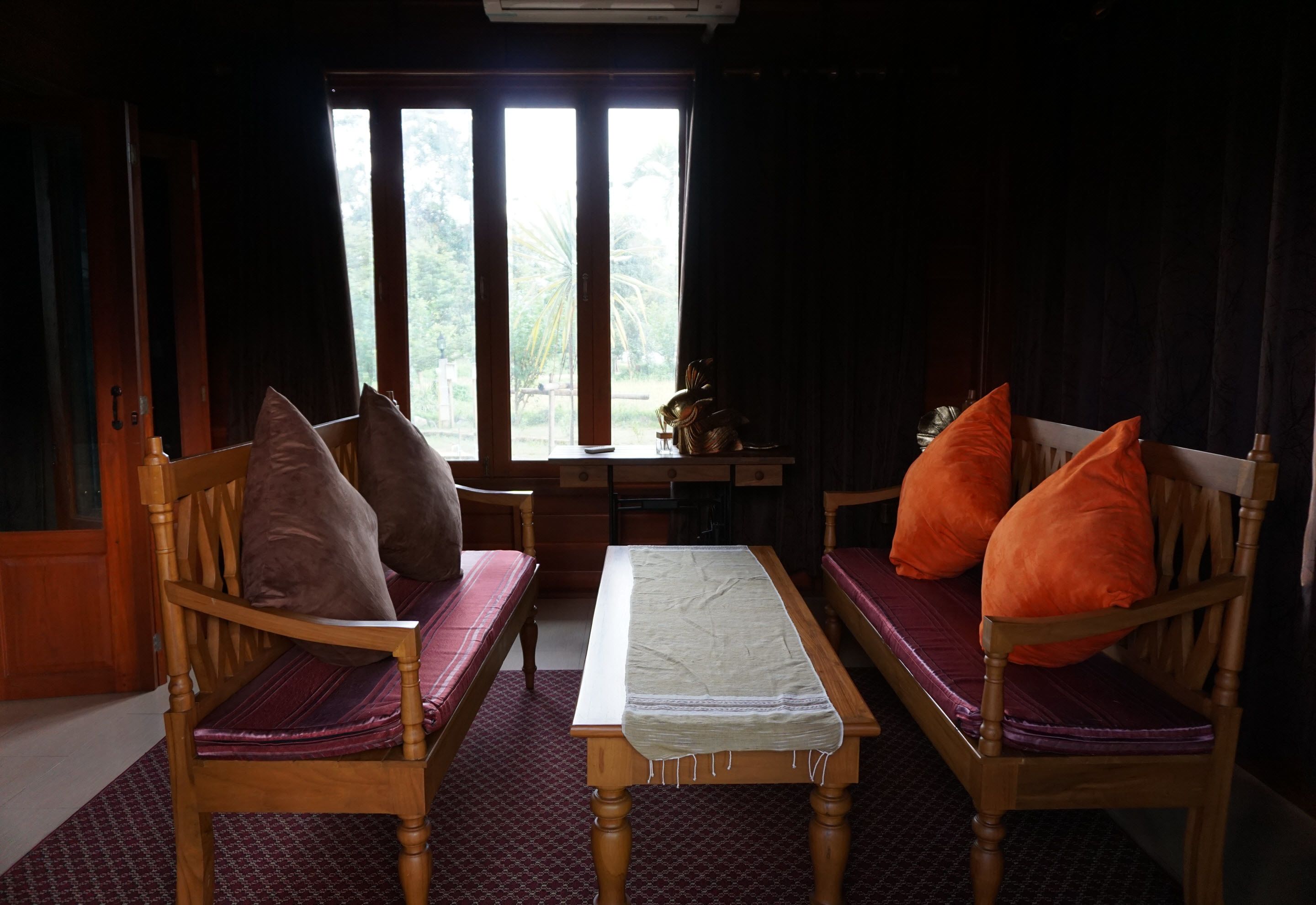 A room with two wooden chairs with purple cushions, a small table with a white cloth, and a view of greenery through a window.