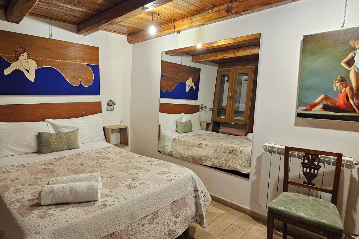 Une chambre à coucher avec un grand lit, deux tables de chevet, une chaise et des œuvres d’art accrochées aux murs.