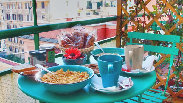 Un balcón con una mesa dispuesta para el desayuno, que incluye un tazón de cereales, una taza y una cesta de pan.