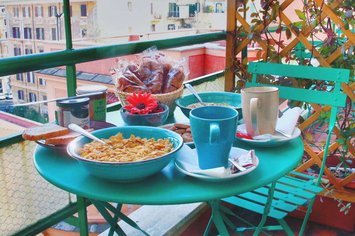 Un balcon avec une table préparée pour le petit-déjeuner, comprenant un bol de céréales, une tasse et un panier de pain.