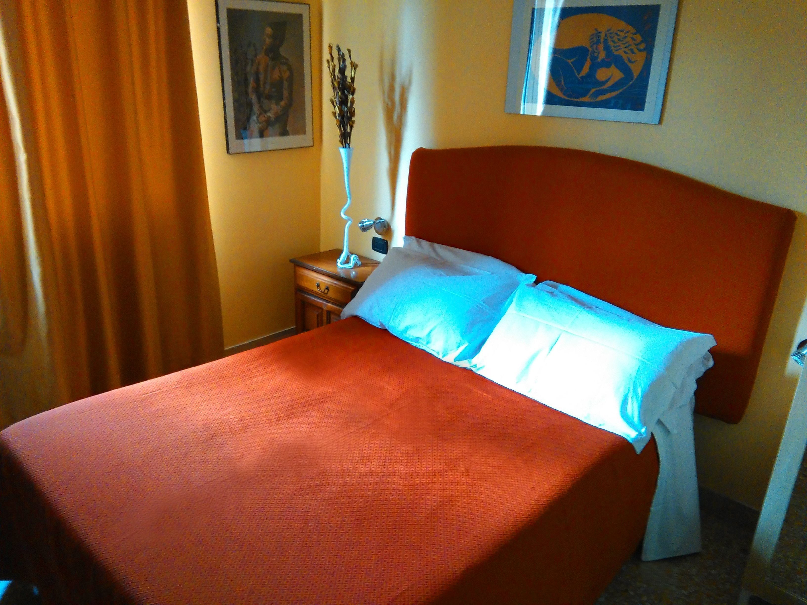 Habitación de hotel con una cama grande, una mesita de noche con lámpara y dos cuadros en la pared.