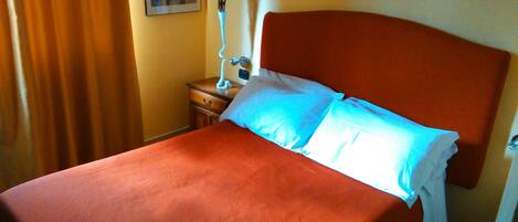 Habitación de hotel con una cama grande, una mesita de noche con lámpara y dos cuadros en la pared.