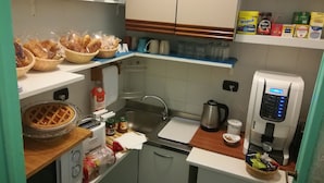 Una cocina compacta con cafetera, hervidor y diversos alimentos en estantes.