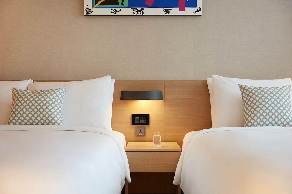 A hotel room with two beds, a nightstand with a lamp, and a painting on the wall.