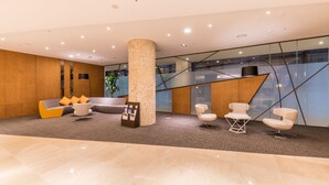 A modern lobby with a central column, seating area, and a glass railing overlooking a lower level. - Howard Johnson by Wyndham Incheon Airport (Incheon)