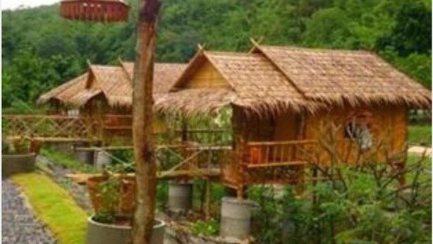 Une rangée de huttes à toits de chaume, avec une structure centrale en bois, le tout entouré de verdure.