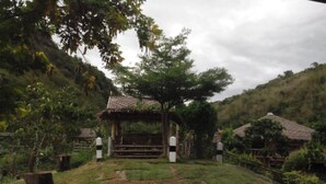 Un espace extérieur rustique agrémenté d’un gazebo en bois, entouré d’arbres et d’une colline verdoyante.