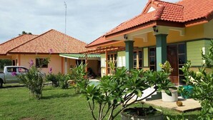 Ein zweigeschossiges Haus mit rotem Ziegeldach, grünen Säulen und einem gepflegten Garten mit verschiedenen Pflanzen.