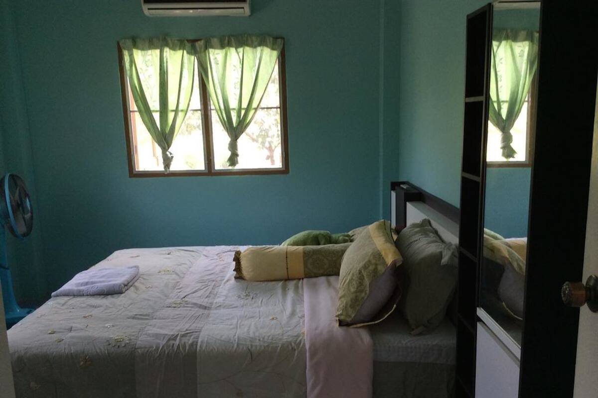 A bedroom with a bed, a window with curtains, an air conditioning unit, and a mirror.