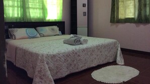 Ein Schlafzimmer mit Bett, Kissen, einem Nachttisch, einem Spiegel und einem Fenster mit grünen Vorhängen.
