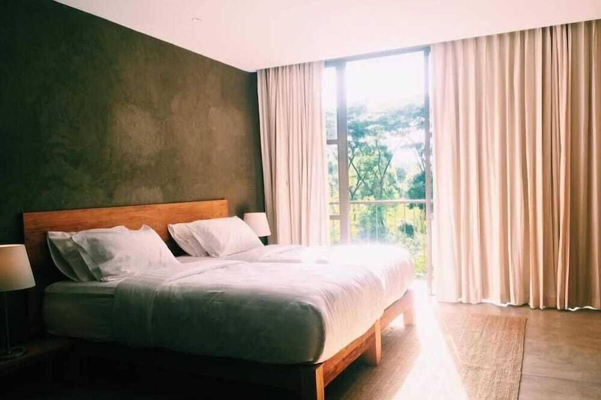 A bedroom with a large bed, a wooden headboard, and a view of greenery through the window.
