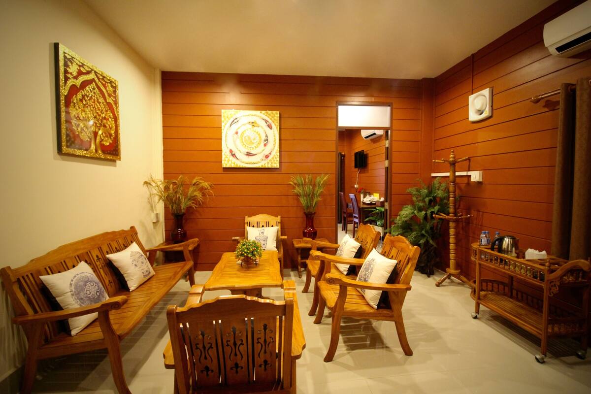 A cozy living room with wooden furniture, a coffee table, and decorative plants.