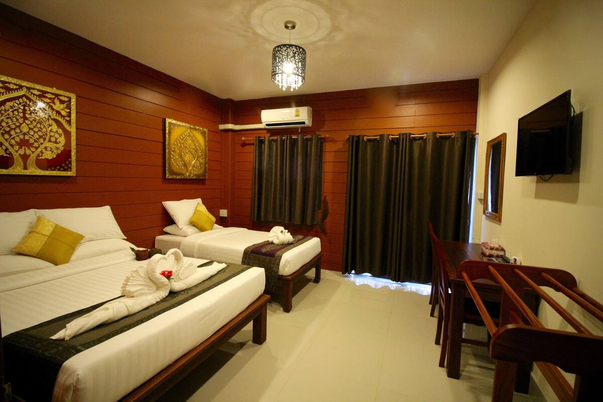 A hotel room with two beds, a dining table, a TV, and an air conditioning unit.