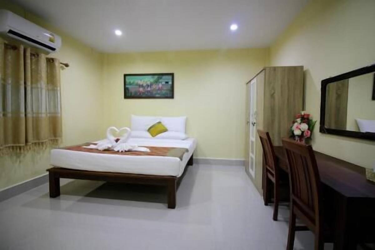A hotel room with a bed, a desk, a chair, an air conditioning unit, a painting on the wall, and a mirror.