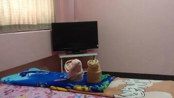 Quarto com paredes cor-de-rosa, cama com colcha de tema alfabético e colorido, televisão em um móvel e ar-condicionado fixado na parede.